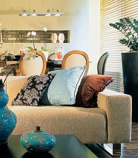 Kolorowe, wzorzyste poduszki kontrastują z surowym ksztaltem i obiciem kanapy.