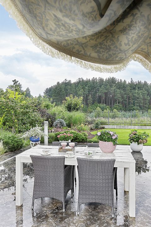 Urządzony naturalnie, sielsko: stół, plecione fotele, kwiaty.